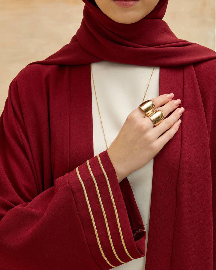 Person wearing a red abaya with gold accents on a beige background